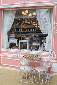 two white chairs and a table in front of a store window with pink paint on it