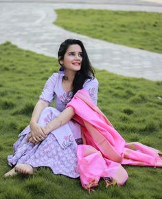 a woman is sitting on the grass with her pink scarf around her neck and looking off into the distance