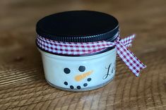 a glass jar with a snowman design on the lid sitting on a wooden table