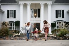 two women holding hands in front of a large house