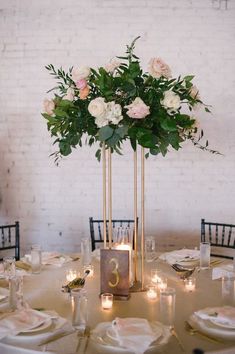 the centerpieces on this table are filled with roses and greenery, while candles stand in front of them