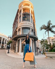 a woman is standing in front of a building holding shopping bags and posing for the camera