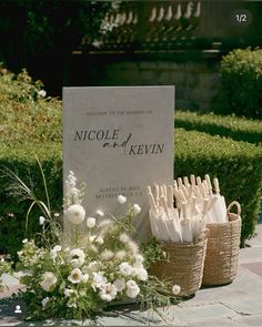 two baskets filled with white flowers next to a sign that reads nicole and kevin