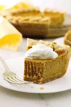 a slice of pumpkin pie on a plate with a fork next to it and another piece of pie in the background