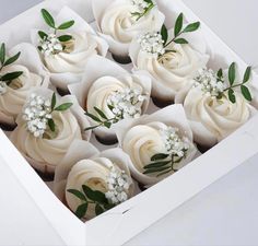 a box filled with cupcakes covered in white frosting and topped with flowers