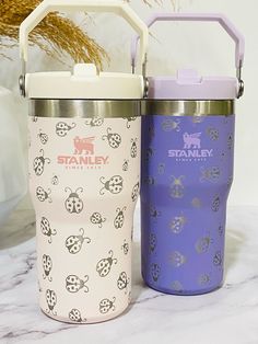 two insulated water bottles sitting next to each other on a marble counter with flowers in the background