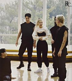 the group of young people are standing together in front of a large window, talking and laughing