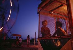 two people sitting in a caged area with ferris wheel in the background at night