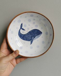 a hand holding a bowl with a whale painted on the side and polka dots around it