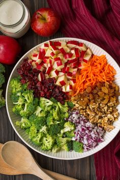 a bowl filled with broccoli, apples, cranberries, and nuts