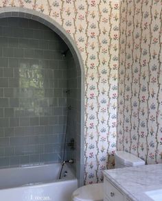 a bath room with a toilet a sink and a tub next to a wall paper