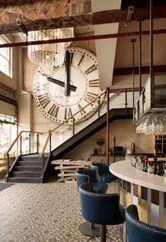 a large clock mounted to the side of a wall in a bar next to stairs