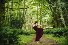 a woman in a red dress is dancing on a dirt path through the woods and trees