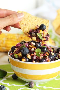 a hand holding a tortilla chip with blueberries and corn on the cob