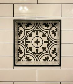 a white tiled wall with a square window in the center and black trim around it