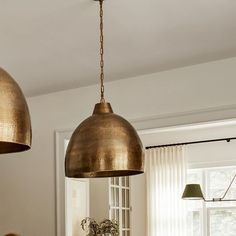 two lights hanging from the ceiling in a kitchen with white walls and wooden table top