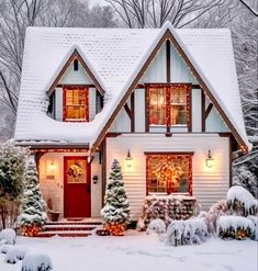 a white house covered in snow with christmas lights on the windows and trees around it