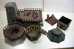 several miniature buildings are shown on a white table top, including one with an umbrella and the other without