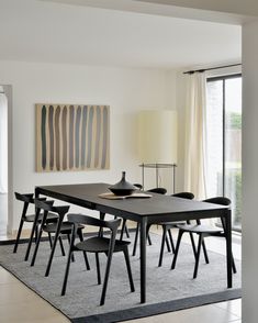 a dining room table with four chairs in front of a large painting on the wall