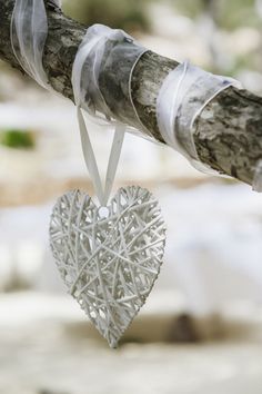 a heart shaped ornament hanging from a tree branch with ribbons on the end