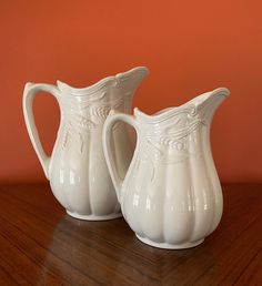 two white pitchers sitting on top of a wooden table