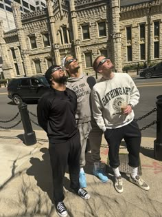 three men standing next to each other on the sidewalk