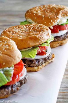 three hamburgers with lettuce, tomato and mayonnaise are lined up on a white paper