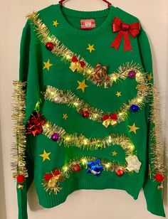 a green christmas sweater with lights and bows on the front is hanging from a wall