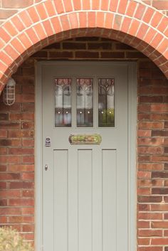 a grey door with three glass panes on the top and bottom, in front of a brick wall