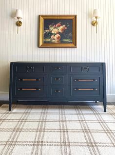 a painting hangs on the wall next to a blue dresser with gold handles and drawers