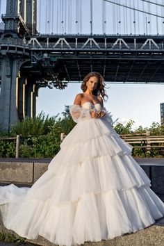 a woman in a white wedding dress standing on the side of a road near a bridge