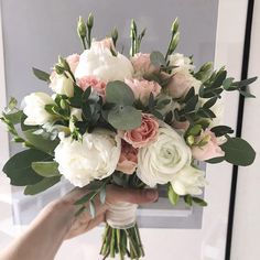 a person holding a bouquet of white and pink flowers with greenery on the stems