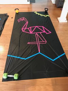 a black kite with pink and blue lines on it sitting on top of a hard wood floor