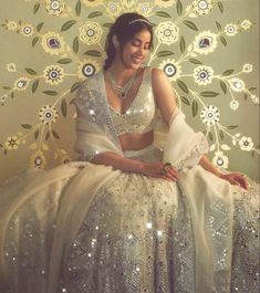 a woman sitting on top of a bed wearing a white dress and diamond necklaces