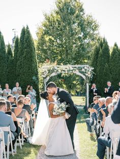 a bride and groom kiss as they walk down the aisle at their outdoor wedding ceremony