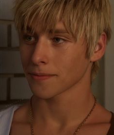 a close up of a person wearing a necklace and looking at the camera with a serious look on his face