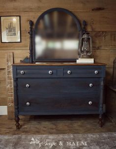 a dresser with a mirror on top of it in front of a wood paneled wall