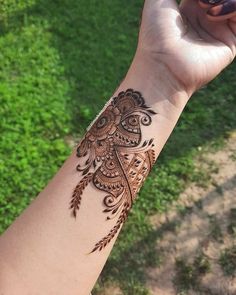 a woman's arm with a henna tattoo on it and green grass in the background