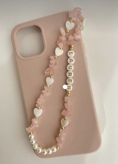 a pink phone case with pearls and heart charms on the front, sitting on a white surface