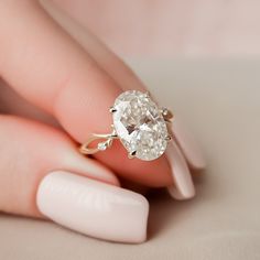 a woman's hand holding an oval diamond ring