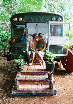 two people sitting in the back of a bus with plants on it and rugs