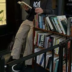 a man sitting on top of a bookshelf next to a pile of books