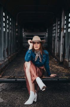 a woman sitting on the back of a truck wearing a hat and dress shirt with white boots