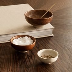 two bowls and a book are sitting on a table with salt and pepper in them