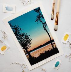 an art project with paint and brushes on the table next to it is a photo of a sunset