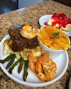 a white plate topped with meat, shrimp and mashed potatoes next to asparagus