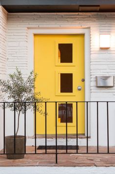 a yellow door is on the side of a white brick building with a black iron fence