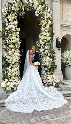 a bride and groom standing in front of a floral arch with white flowers on it