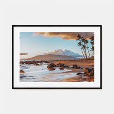 a framed photograph of the beach with palm trees and mountains in the background at sunset