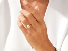 a close up of a person wearing a white shirt holding a gold ring with a diamond on it